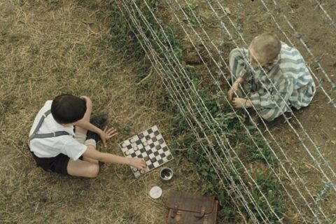 The Boy in Striped Pajamas 2008 Movie Scene Asa Butterfield as Bruno playing chess with Jack Scanlon as Shmuel as they're separated by the barb wire of the concentration camp