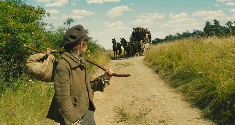 Oliver Twist 2005 Movie Scene Barney Clark as Oliver Twist walking down the country road with a carriage behind him