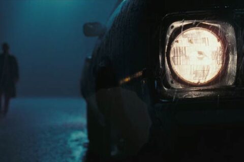 The Hitcher 2007 Movie Scene The headlights of a car with a dark figure of a man in the background