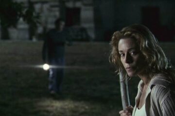 The Orphanage 2007 Movie Scene Belén Rueda as Laura holding a stick and exploring the courtyard at night after she heard a sound