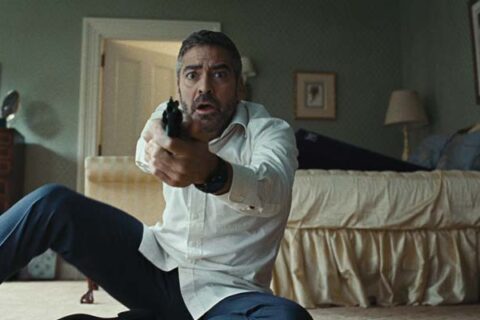 Burn After Reading 2008 Movie Scene George Clooney as Harry Pfarrer holding his gun in the bedroom with the purple ramp seen in the background on the bed, it's a sex toy Liberator Shape