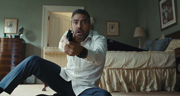 Burn After Reading 2008 Movie Scene George Clooney as Harry Pfarrer holding his gun in the bedroom with the purple ramp seen in the background on the bed, it's a sex toy Liberator Shape