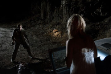 Dark Country 2009 Movie Scene Thomas Jane as Dick holding a rock while Lauren German as Gina is standing next to a car