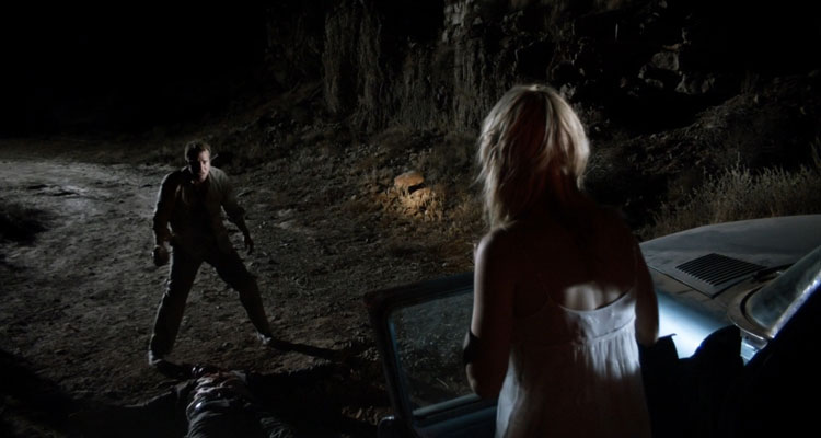 Dark Country 2009 Movie Scene Thomas Jane as Dick holding a rock while Lauren German as Gina is standing next to a car