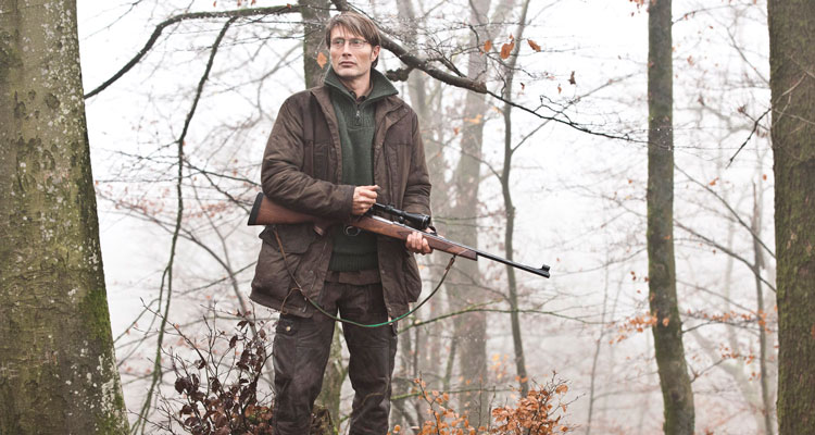 Jagten AKA The Hunt 2012 Movie Mads Mikkelsen as Lucas standing in a forest holding a sniper rifle looking at deer scene