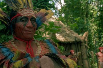 The Serpent and the Rainbow 1988 Movie Amazon shaman wearing bright and colorful feathers smiling as Bill Pullman is hallucinating