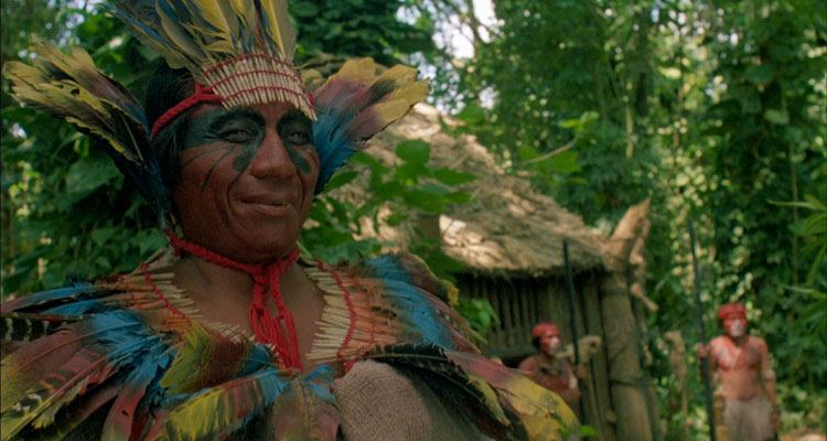 The Serpent and the Rainbow 1988 Movie Amazon shaman wearing bright and colorful feathers smiling as Bill Pullman is hallucinating