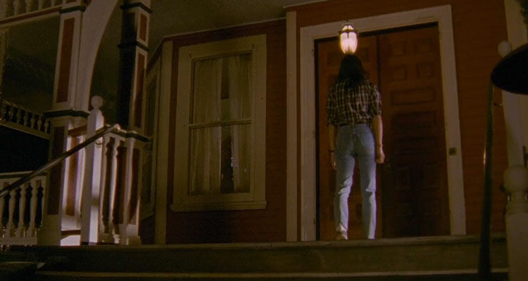 The House of the Devil 2009 Movie Jocelin Donahue in jeans and plaid shirt looking towards the door of the house