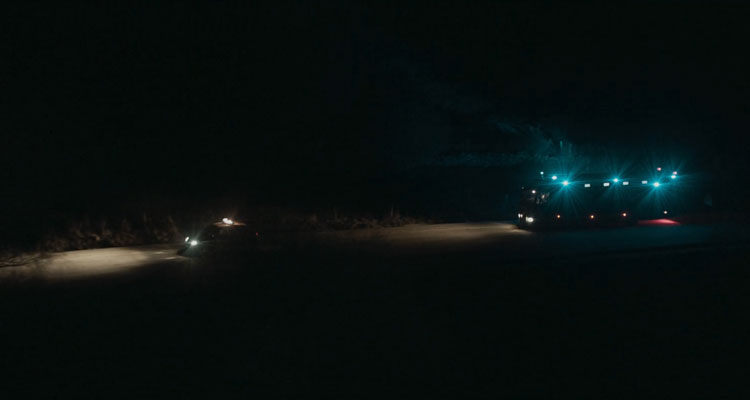 Bajocero 2021 Movie A police car in front of an armored prisoner transport van on a dark road