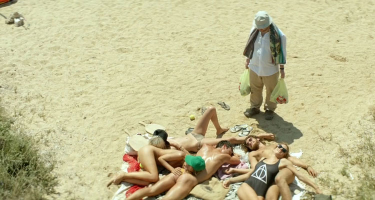 Suntan 2016 Movie Makis Papadimitriou as Kostis holding bags of beer on the beach in front of the gang