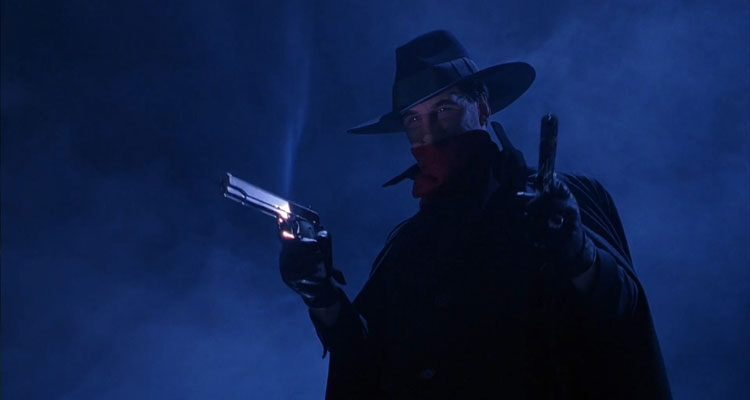 The Shadow 1994 Movie Scene Alec Baldwin as Lamont Cranston AKA The Shadow holding two guns with a hat and red bandana on the bridge