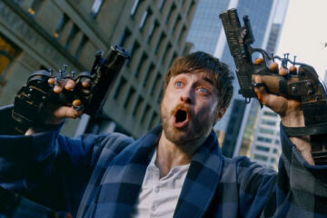Guns Akimbo 2019 Movie Scene Daniel Radcliffe as Miles in his bathrobe waving guns bolted to his hands and screaming at police