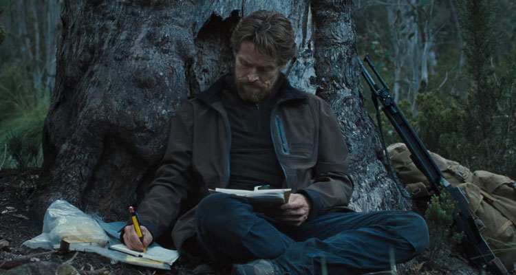 The Hunter 2011 Movie Scene Willem Dafoe as Martin sitting next to a huge tree in the forest and taking notes