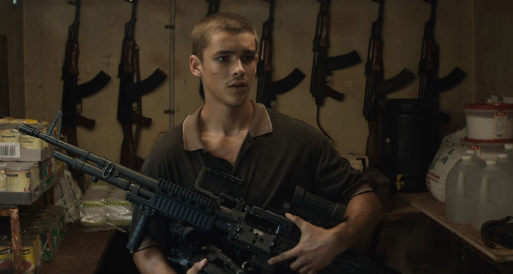 Son of a Gun 2014 Movie Scene Brenton Thwaites as JR holding a heavy machinegun with AK-47 behind him