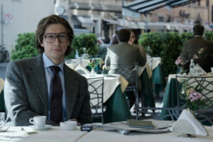 House of Gucci 2021 Movie Scene Adam Driver as Maurizio Gucci drinking espresso and smoking in a coffee shop