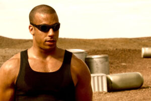 Pitch Black 2000 Movie Scene Vin Diesel as Riddick standing in the scorching sun wearing eye protection and a sleeveless shirt showing off his huge muscles