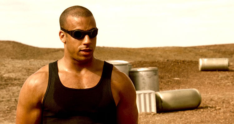 Pitch Black 2000 Movie Scene Vin Diesel as Riddick standing in the scorching sun wearing eye protection and a sleeveless shirt showing off his huge muscles