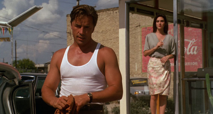 The Hot Spot 1990 Movie Scene Don Johnson as Harry Madox wearing a white sleeveless shirt at the car lot with Jennifer Connelly as Gloria smoking a cigarette in the background