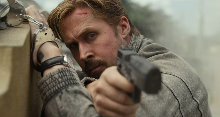 The Gray Man Movie 2022 Scene Ryan Gosling as Six holding a gun while handcuffed to a post