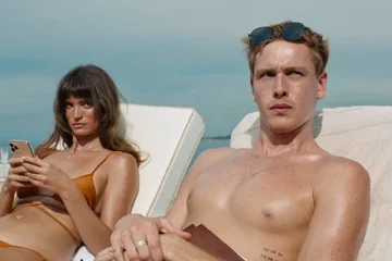 Triangle of Sadness 2022 Movie Scene Harris Dickinson as Carl and Charlbi Dean as Yaya sunbathing on top of a luxury yacht