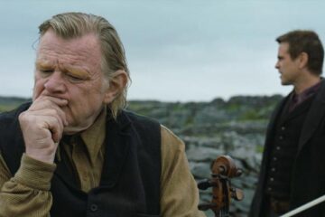 The Banshees of Inisherin 2022 Movie Scene Brendan Gleeson as Colm holding his violin and thinking with Colin Farrell as Padraic standing in the background