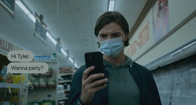 Sick 2022 Movie Scene Joel Courtney as Tyler wearing a surgical mask and reading the messages sent by the killer