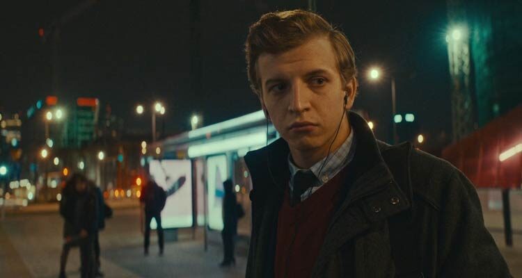 The Hater 2020 Movie Scene Maciej Musialowski as Tomasz Giemza waiting for a bus while wearing headphones