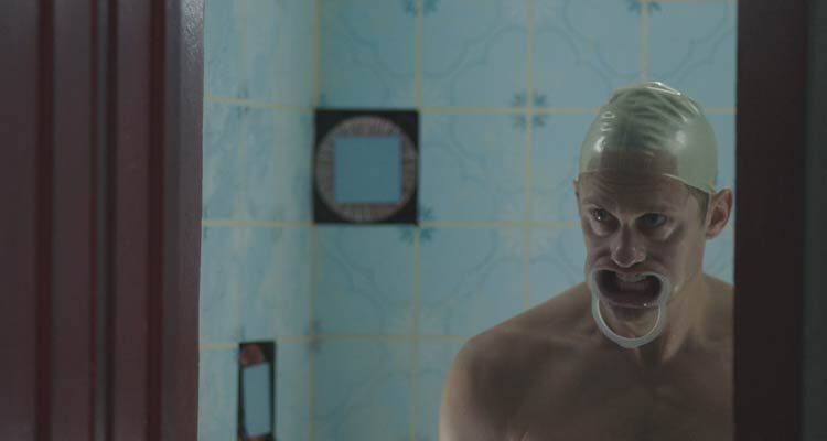 Infinity Pool 2023 Movie Scene Alexander Skarsgård James wearing a swimming cap and a mouth prop in the duplication chamber or a pool filled with strange liquid