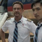 Plane 2023 Movie Scene Gerard Butler as Brodie Torrance and Yoson An as Samuel Dele standing in front of a plane that's just crash landed in the jungle