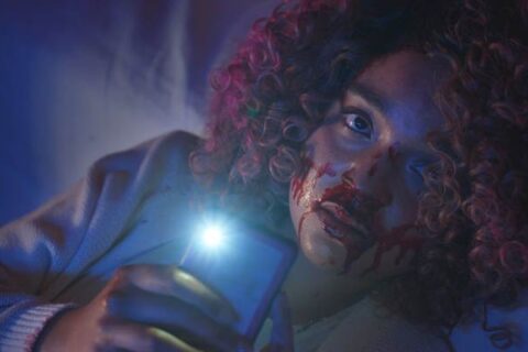 Sissy 2022 Movie Scene Aisha Dee as Cecilia holding her phone and filming the murder with a bloody face