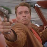 Last Action Hero 1993 Movie Scene Arnold Schwarzenegger as Jack Slater driving a car and shooting his desert eagle gun at the bad guys