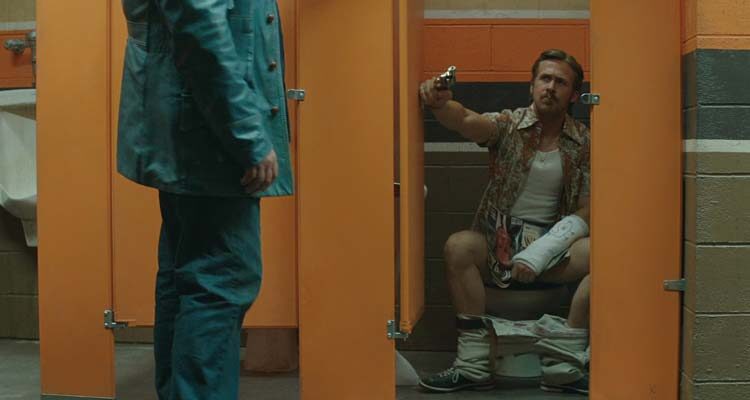 The Nice Guys 2016 Movie Scene Ryan Gosling as Holland March sitting on the toilet with an arm in cast, holding a gun and smoking a cigarette when Russell Crowe as Jackson Healy bursts in