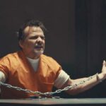 Nefarious 2023 Movie Scene Sean Patrick Flanery as Nefarious AKA Edward Wayne Brady in an orange prison jumpsuit in handcuffs spreading his arms