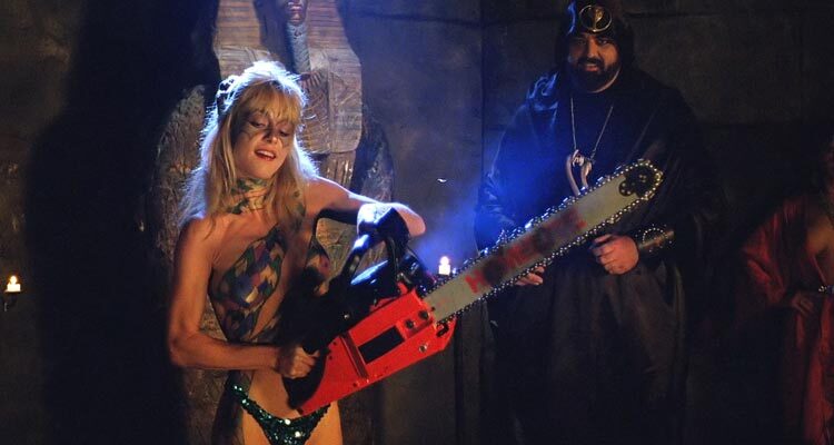Hollywood Chainsaw Hookers 1988 Movie Scene Linnea Quigley as Samantha after The Virgin Dance of the Double Chainsaws holding a chainsaw with Gunnar Hansen as the cult leader cheering her in the background