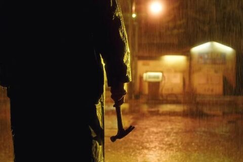 Open 24 Hours 2018 Movie Scene A killer in a raincoat holding a hammer in the rain in front of a remote gas station