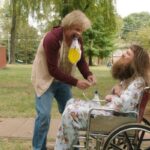 Dumb and Dumber To 2014 Movie Scene Jeff Daniels as Harry holding a catheter bag full of piss in his mouth while he fixes another one for Jim Carrey as Lloyd