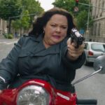 Spy 2015 Movie Scene Melissa McCarthy as Susan Cooper holding a gun while driving a scooter