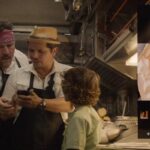 Chef 2014 Movie Scene Jon Favreau as Carl Casper and his son looking at John Leguizamo as Martin's phone with a picture of a delicious sandwich