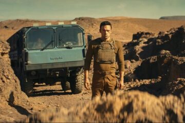 The Wages of Fear 2024 Movie Scene Alban Lenoir as Alex standing in front of a big rock with the truck carrying nitroglycerine in the background